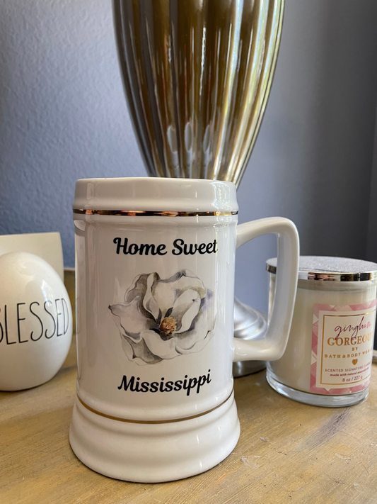 Product is front & center, with light reflecting off its ceramic surface.In the background is the base of a ribbed silver lamp, a white candle with pink label & a decorative egg with the text "BLESSED"